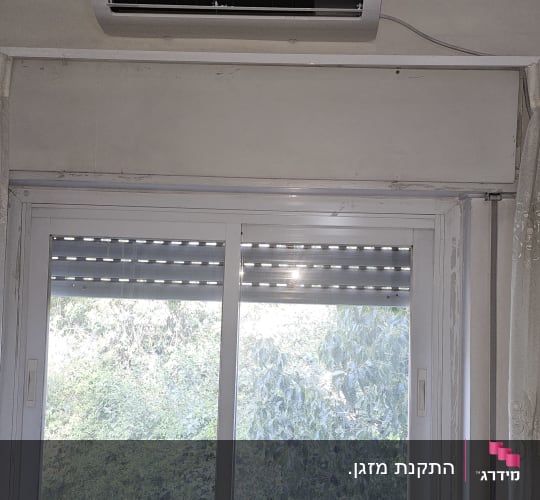 מזגן מותקן מעל חלון עם נוף ירוק בחוץ